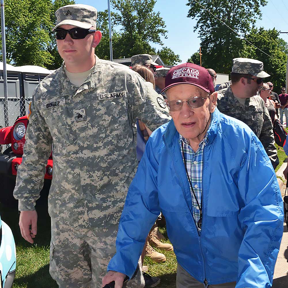 Elderly vet with walker escorted by younger serviceman.